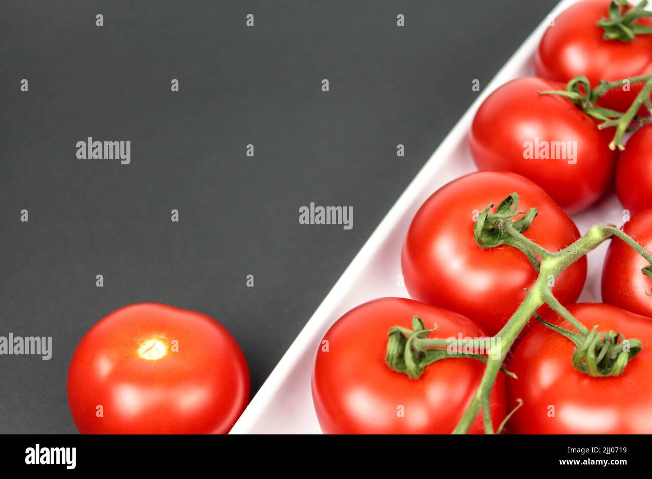 Red tomatoes on white plate on black background Stock Photo