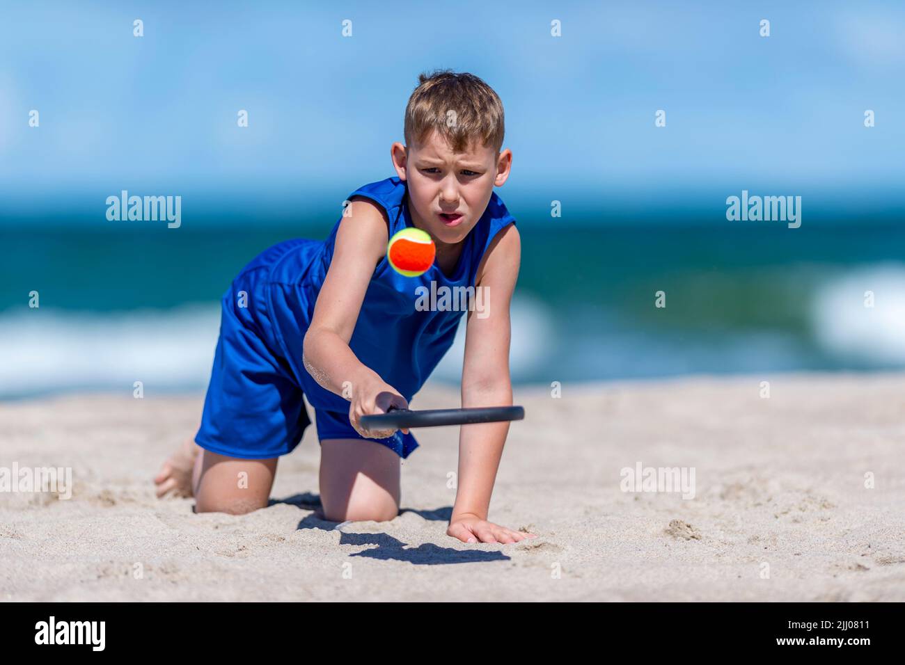 Young boy playing tennis on beach. Kids sport concept. Horizontal sport theme poster, greeting cards, headers, website and app Stock Photo