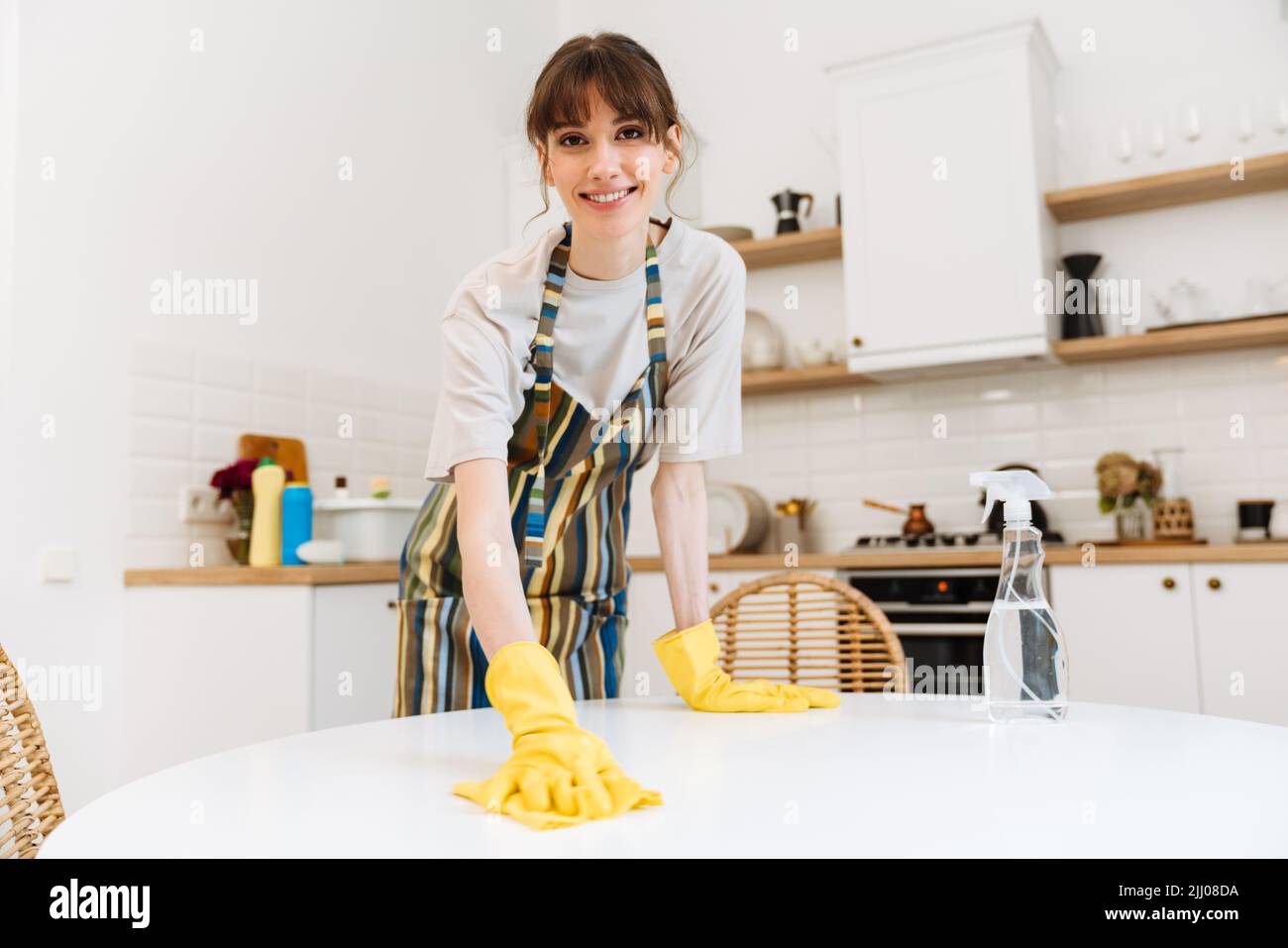 White young woman in gloves smiling while cleaning table at home Stock