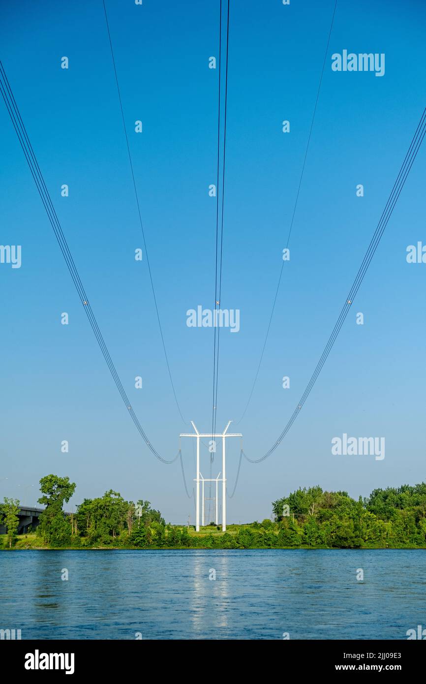 Columns of modern electric power distribution poles with cables crossing a river in a rural region. Stock Photo