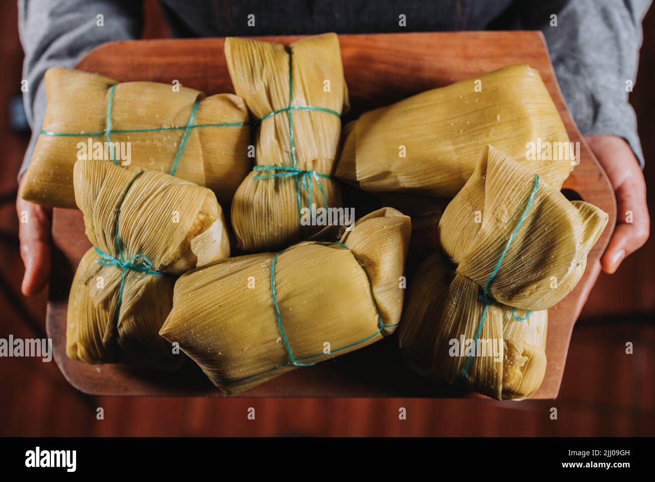 woman's hands holding chilean homemade humitas. Ground corn mix wrapped in corn husks and boiled Stock Photo