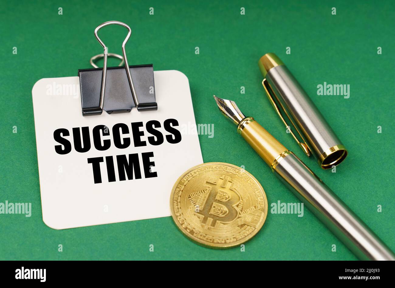 Cryptocurrency and business concept. On a green surface, a bitcoin coin, a pen and a sheet of paper with the inscription - Success time Stock Photo