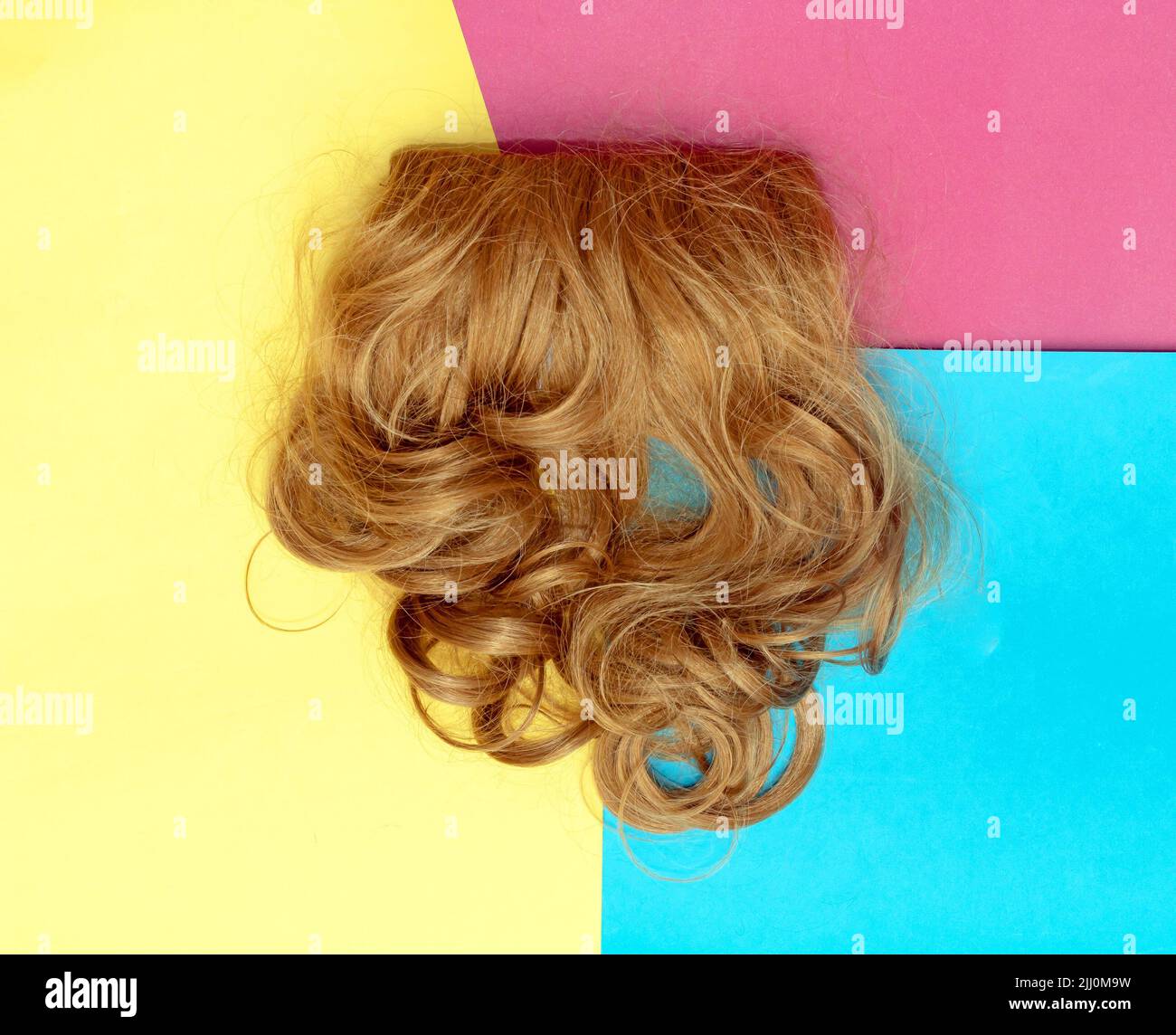 Dark blonde large curls hair extensions wig on colorful background Stock Photo
