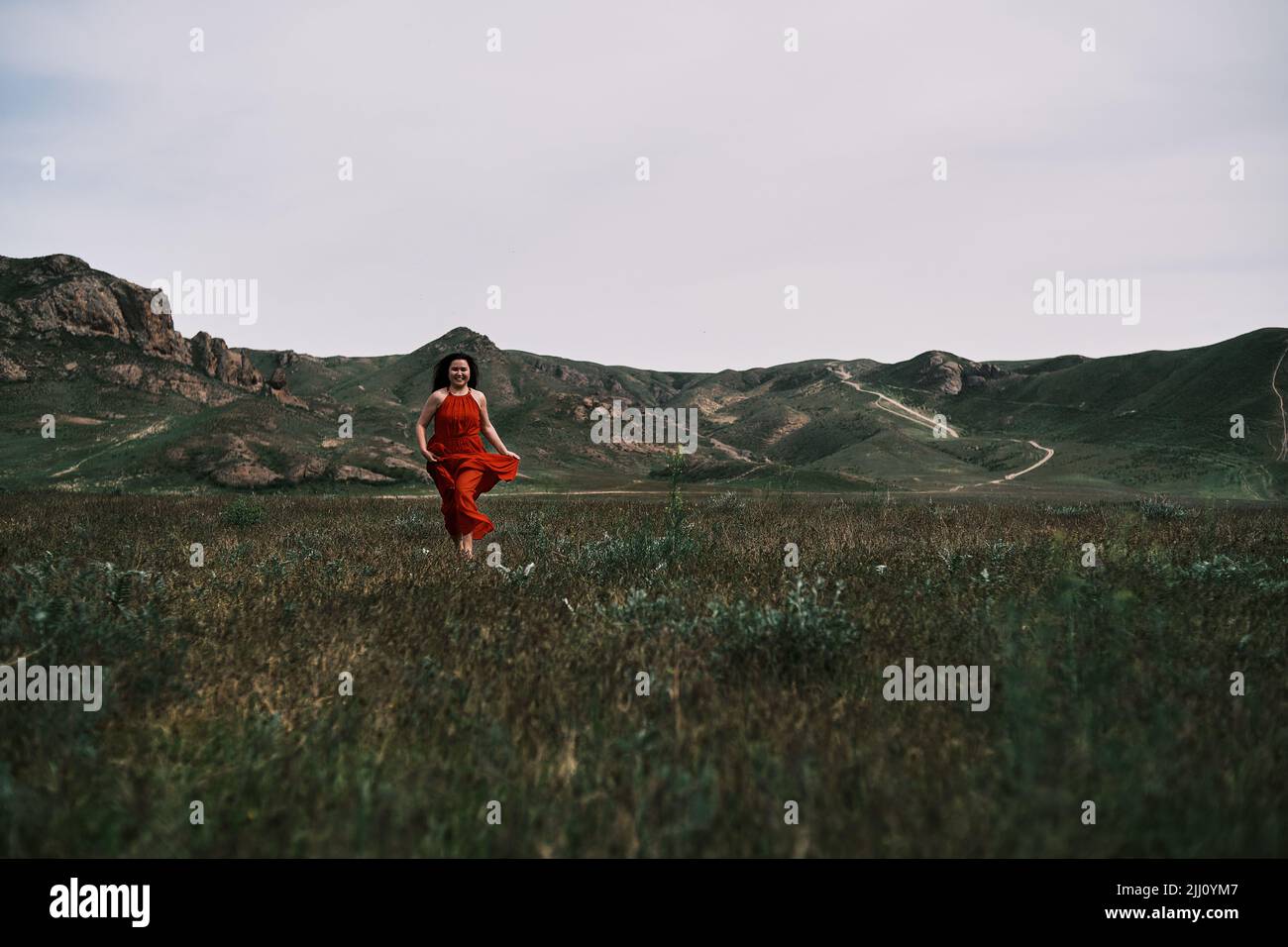 A girl in a red dress running on the field, mountains Stock Photo - Alamy