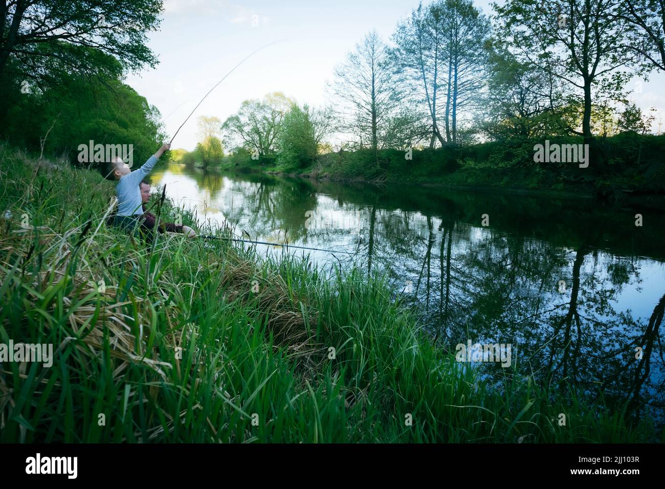 Son and father are fishing on the river bank Stock Photo