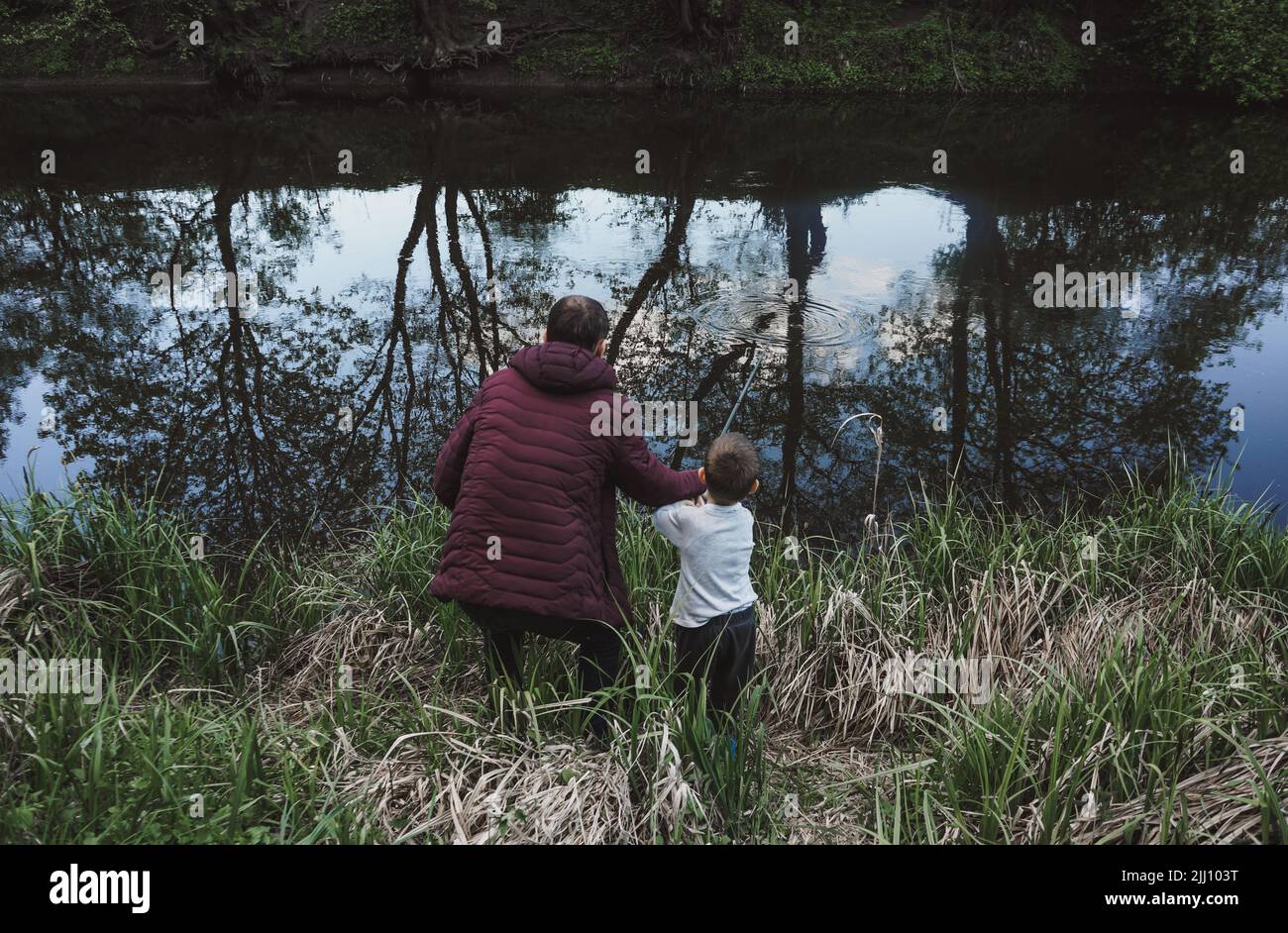 Rear view of father and son fishing on river shore Stock Photo