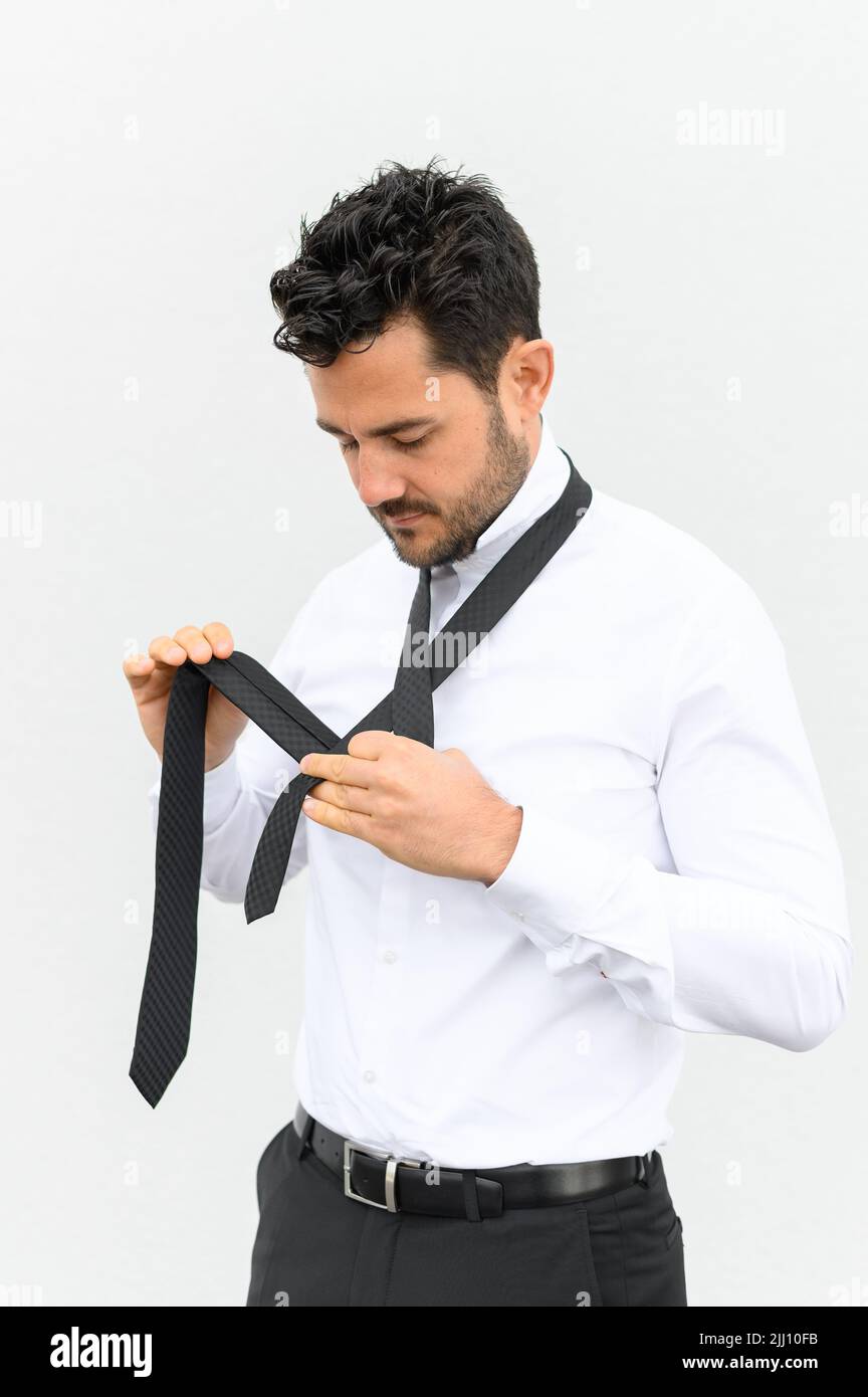 Businessman making a tie knot in front of a white backdrop Stock Photo