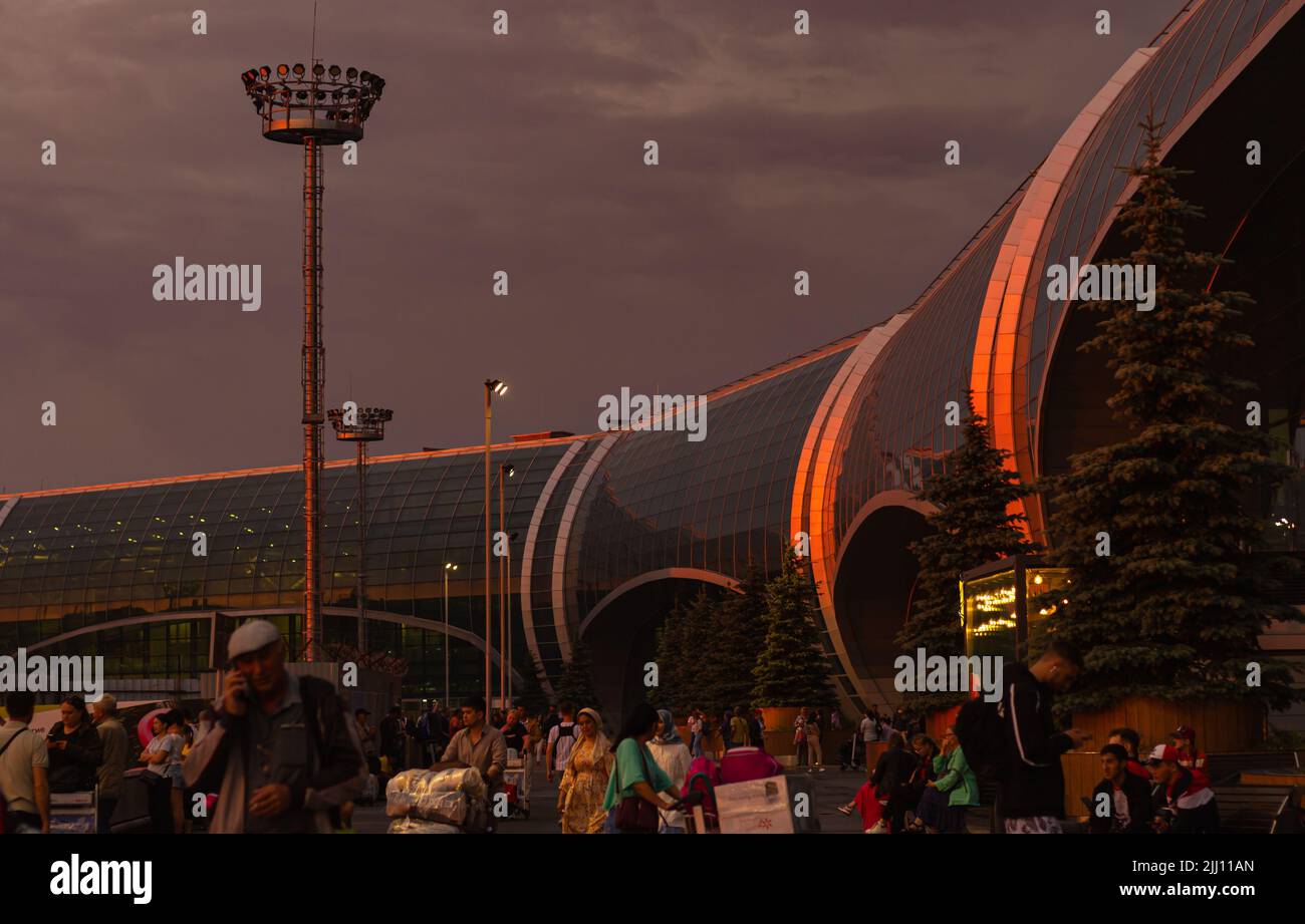 multinational crowd in blur, outdoors on glass and steel terminal international airport background.Vivid building with reflection of colorful orange a Stock Photo