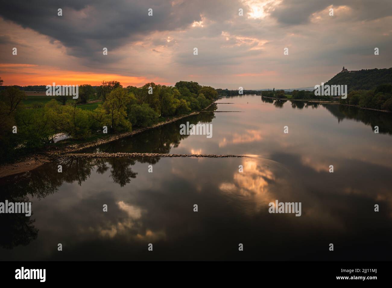 A beautiful view of a lake and a field with trees under the cloudy sky ...