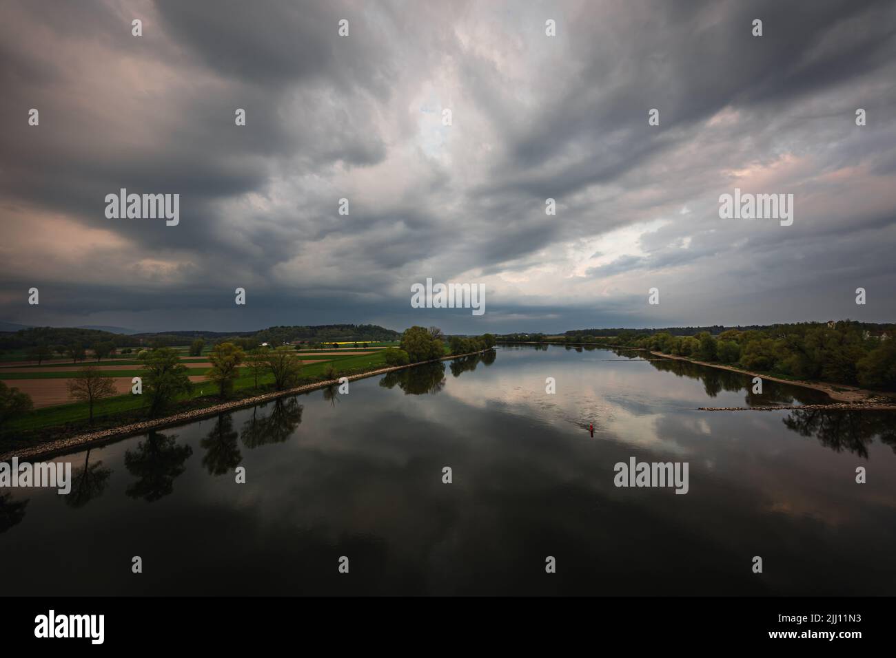A beautiful view of a lake and a field with trees under the cloudy sky ...