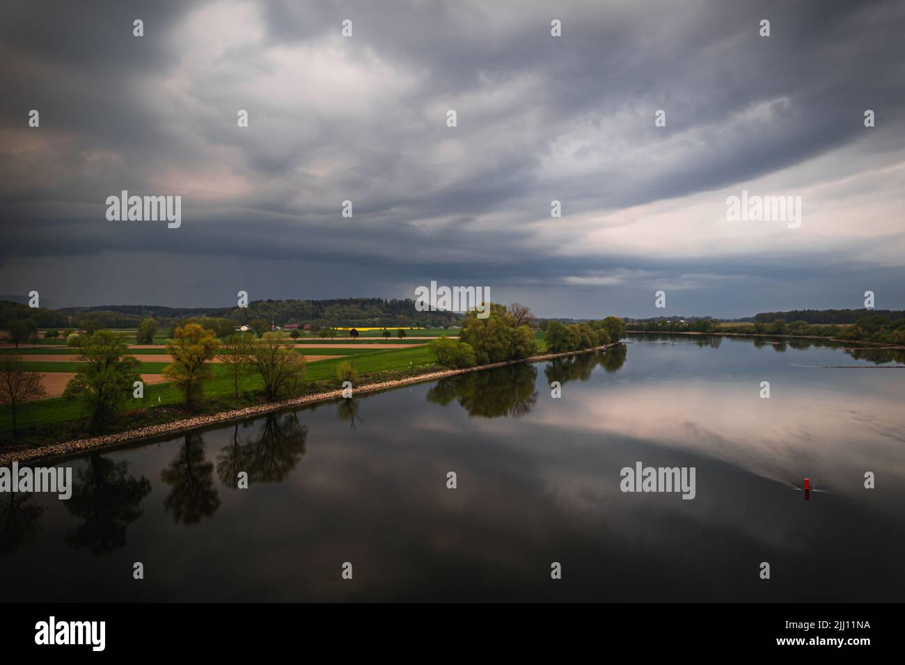 A beautiful view of a lake and a field with trees under the cloudy sky ...