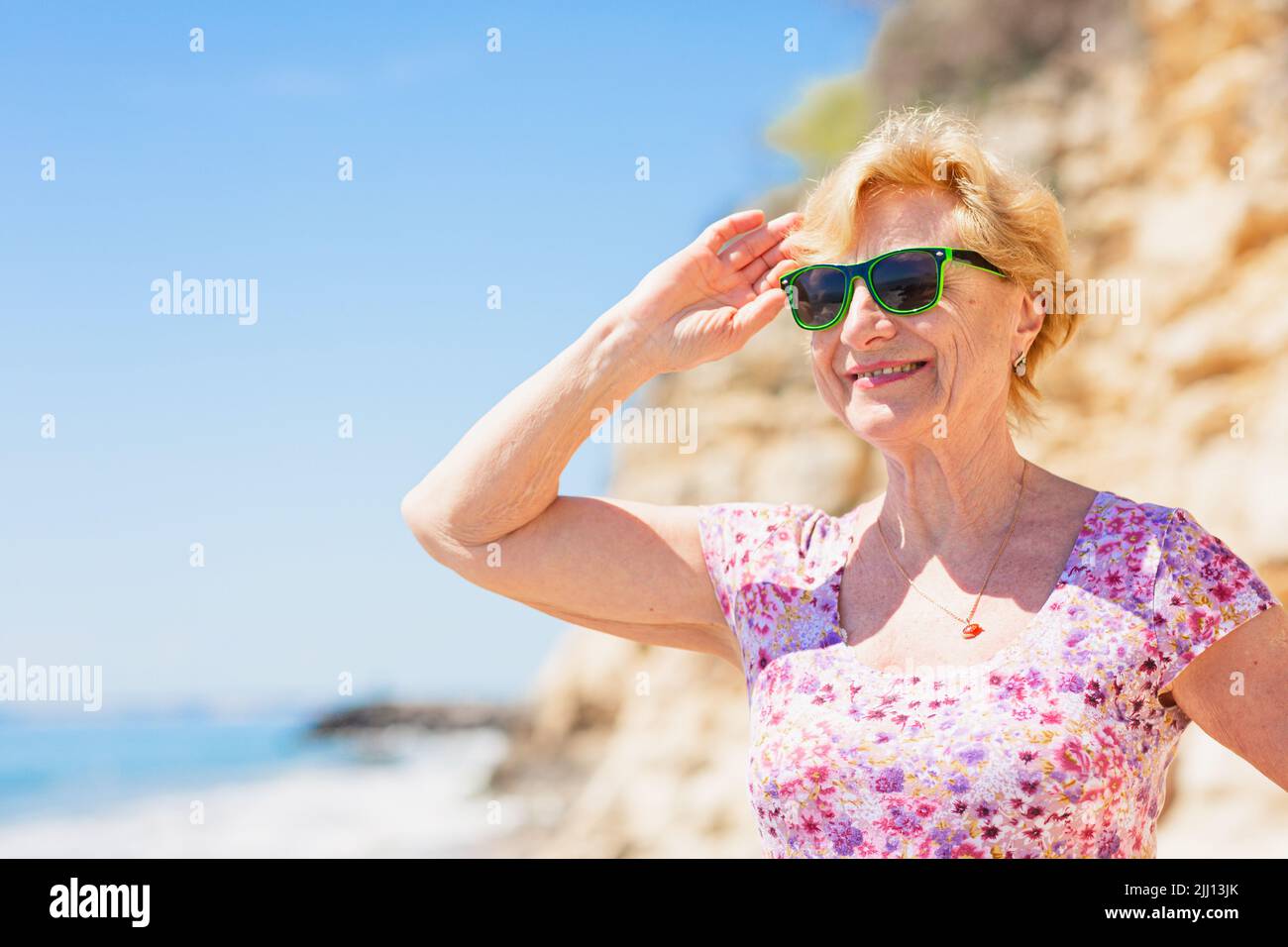 Elderly woman in sunglasses looking at the sea and having fan. Stock Photo
