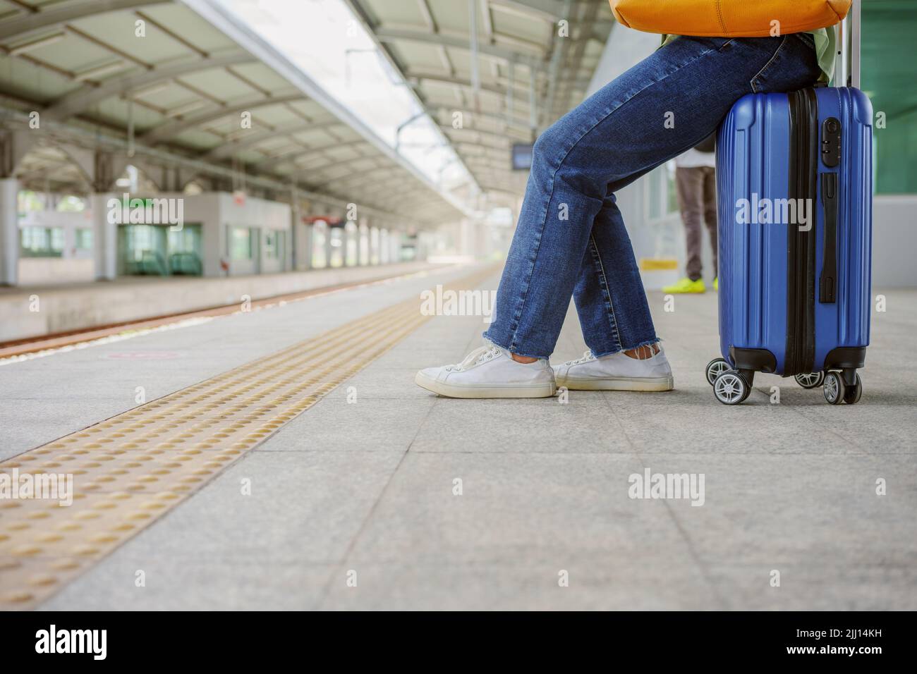 Woman sitting on the bag and waiting at the platform in sky train station. Stock Photo