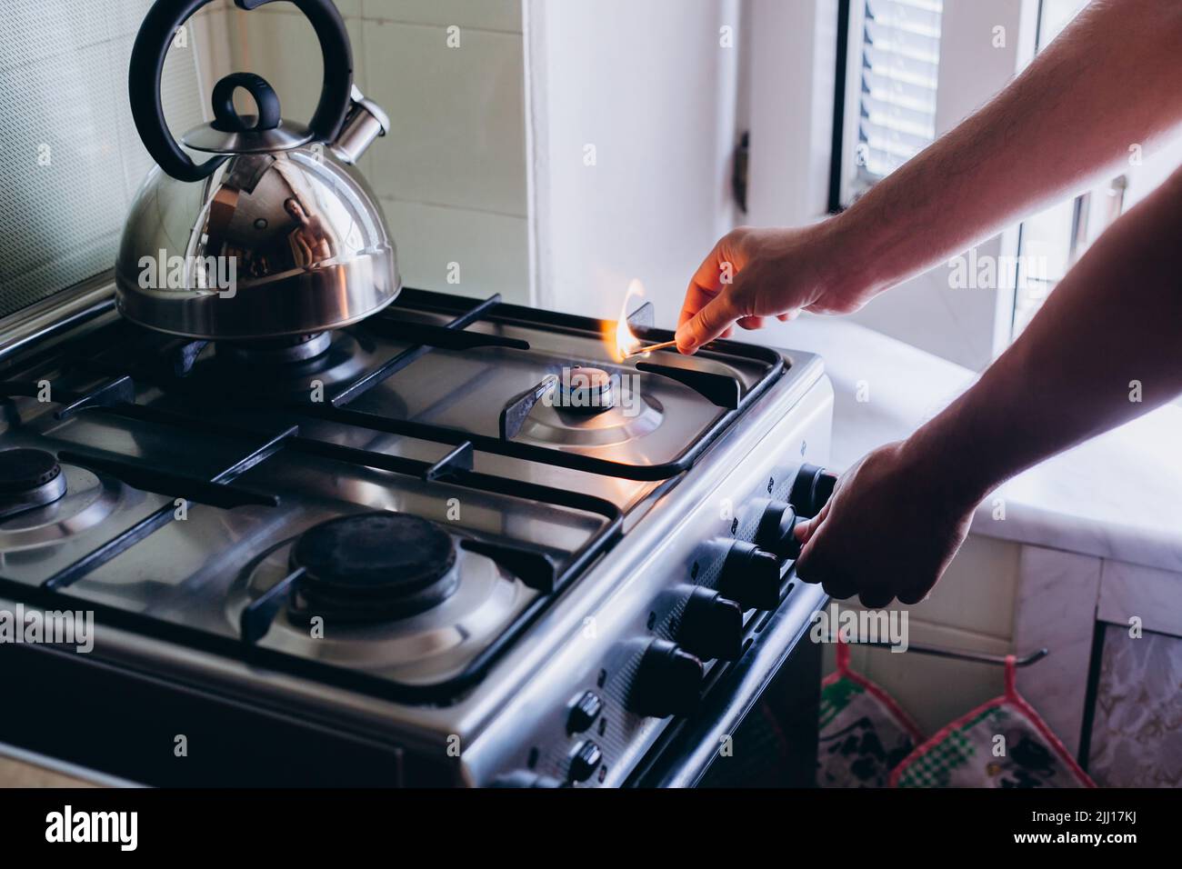 A man's hand with a match lights a gas burner or a gas stove in the
