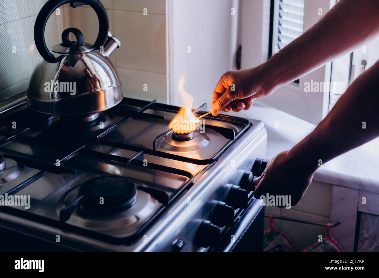 A man's hand with a match lights a gas burner or a gas stove in the