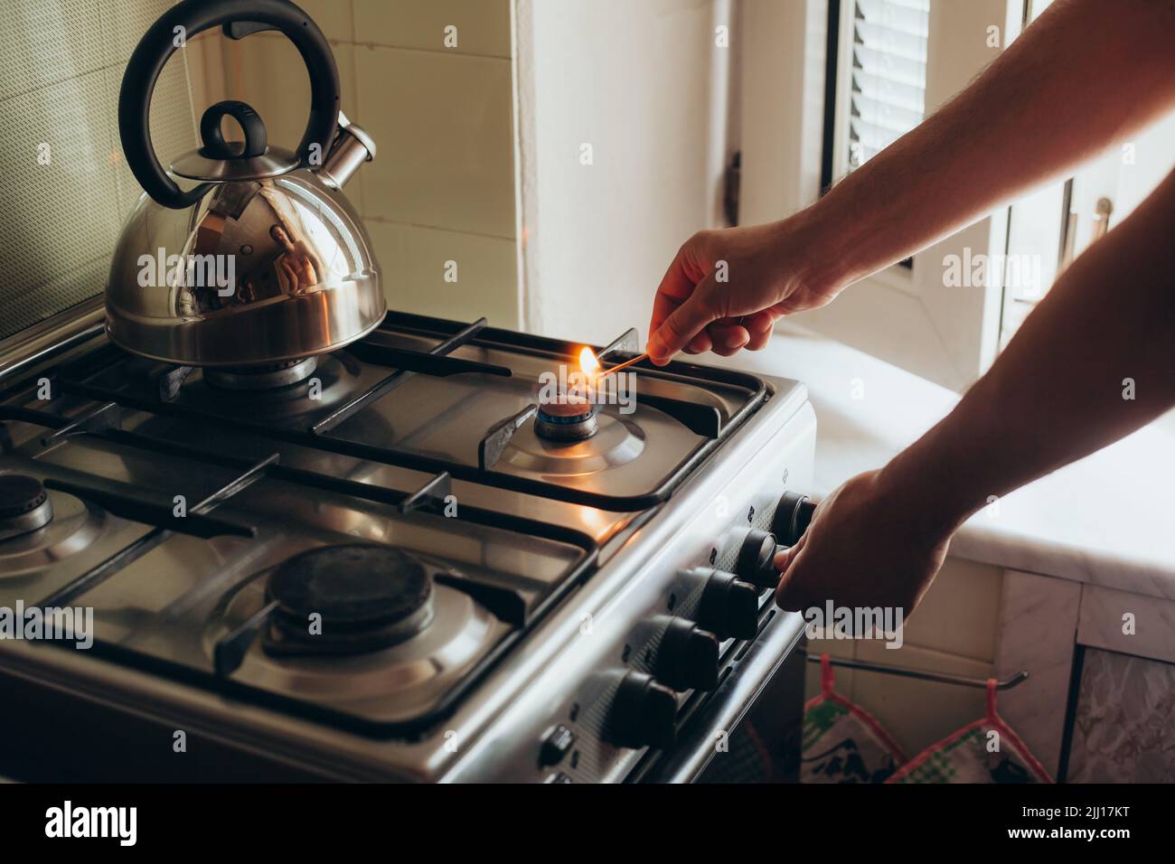 A man's hand with a match lights a gas burner or a gas stove in the
