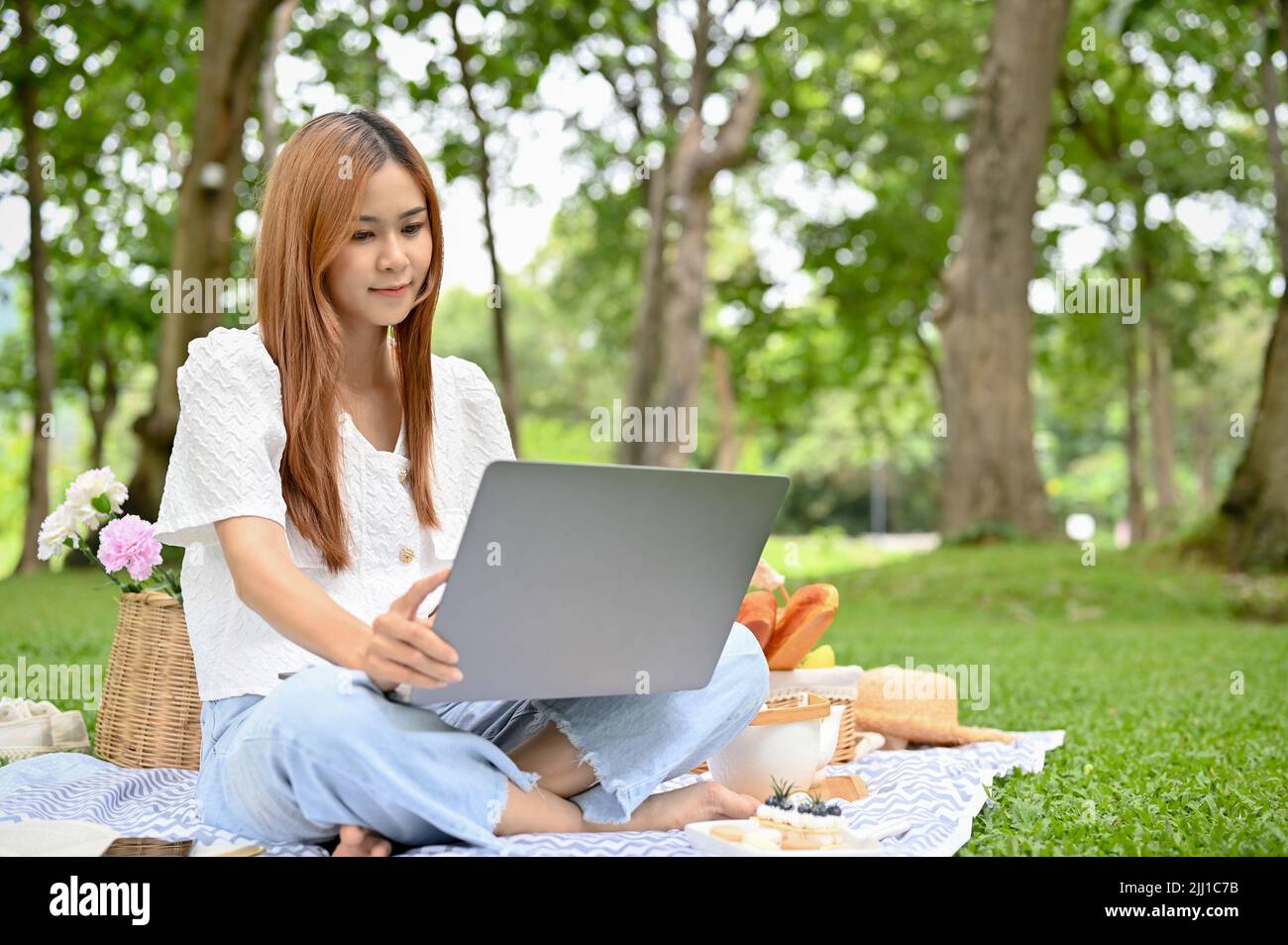 Attractive young Asian female picnicking in the park, sitting on her