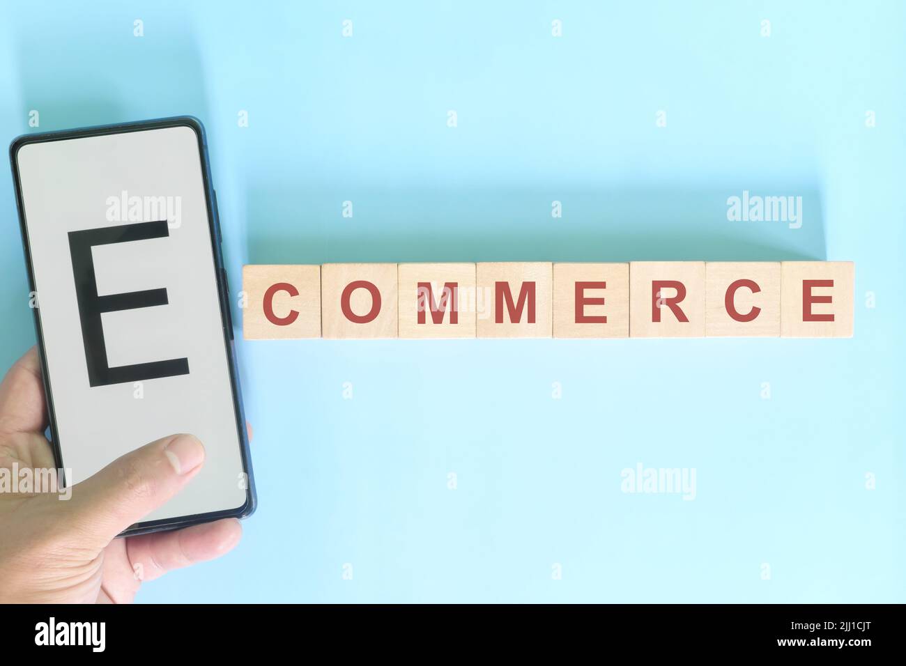 E-commerce business concept. Hand holding mobile phone with word on wooden blocks flat lay in blue background. Stock Photo