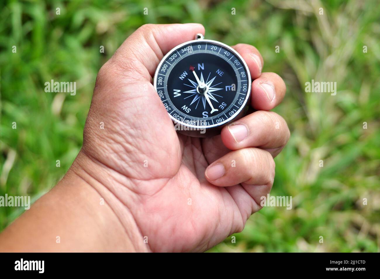 Holding navigation compass close up green leaves background Stock Photo