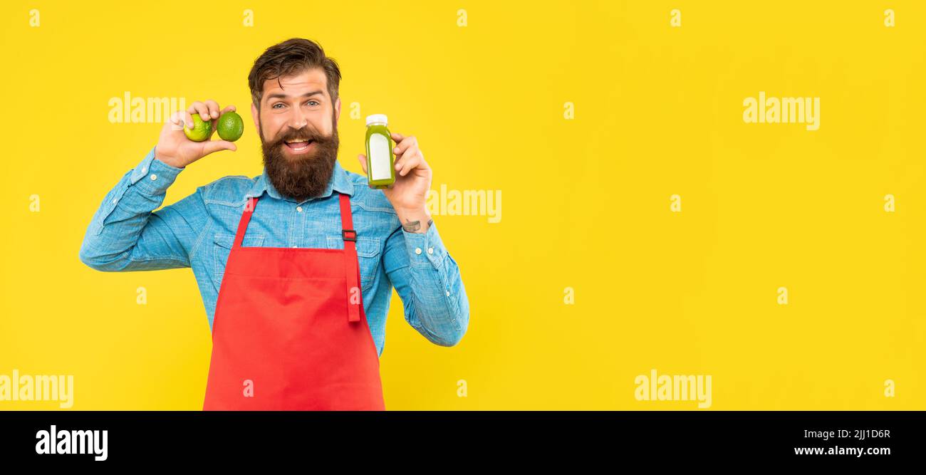 Happy man in apron holding limes and juice bottle yellow background copy space, juice barkeeper Stock Photo