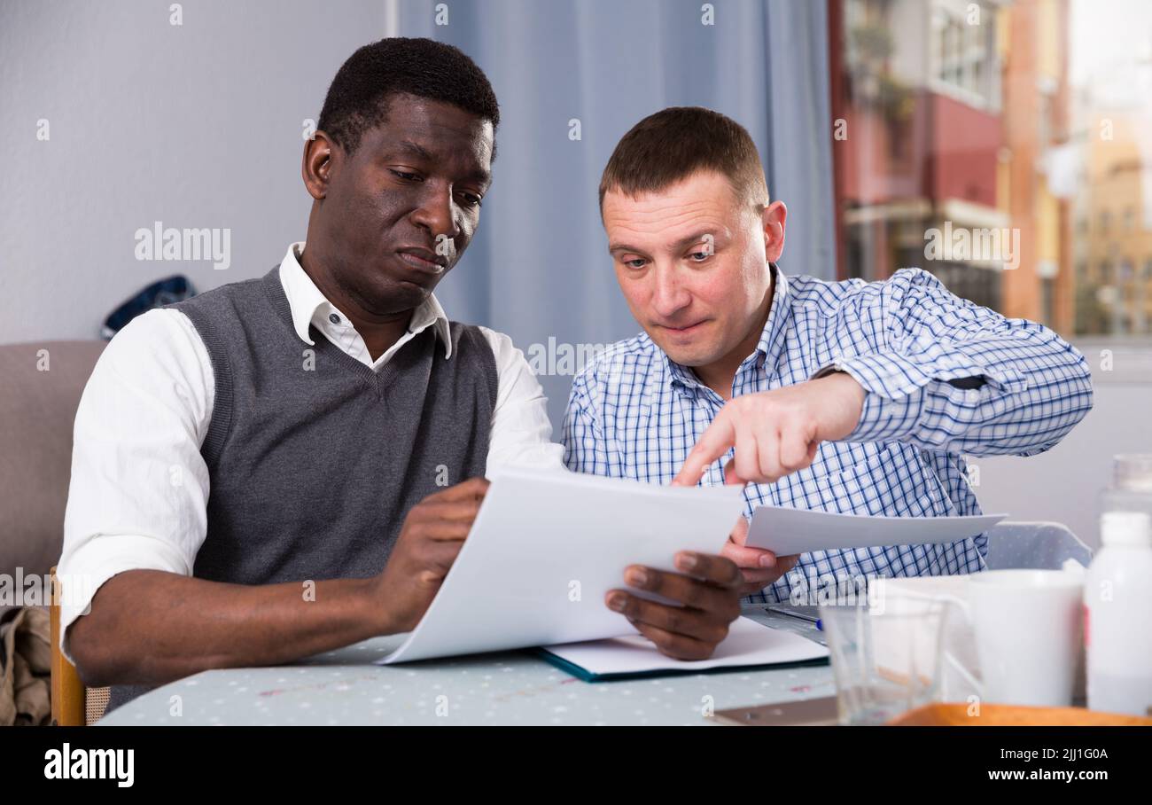 Serious man wit friend discussing documents at home Stock Photo