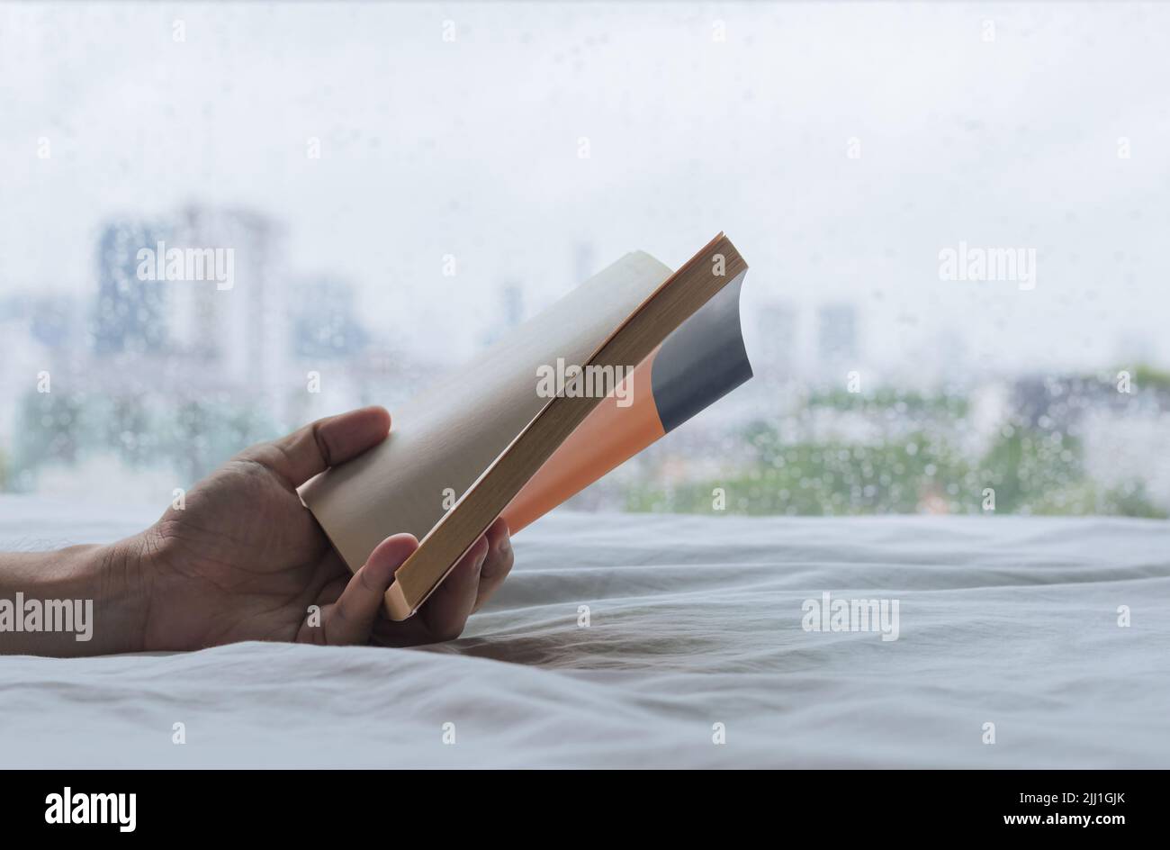 Hand holding a book that reading on bed when rainy day. Stay home and