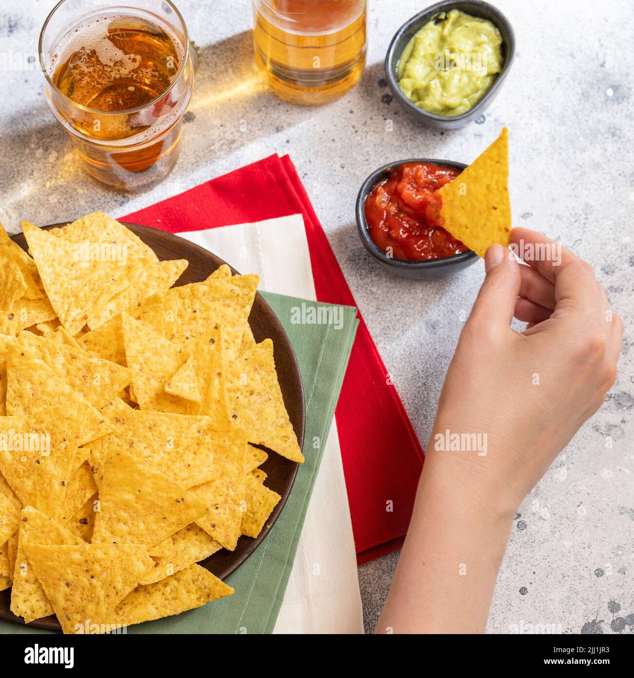Female hand hold one of nachos, Mexican snack served with traditional