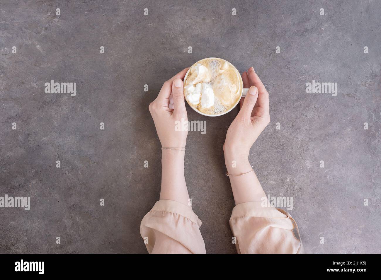 Female hands in silk blouse holding a cup of coffee with whipped cream ...
