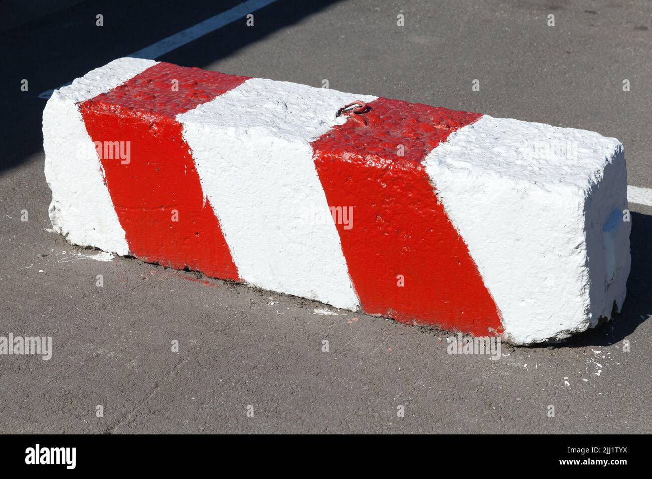 Concrete road block with warning red white diagonal striped pattern lays on an urban road Stock Photo