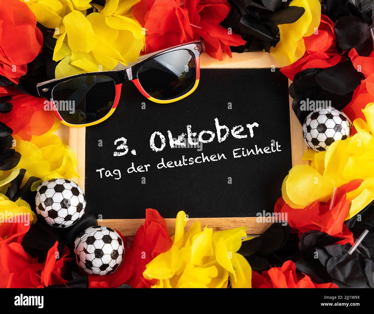 A blackboard with a text saying German Unity Day, balls, sunglasses, and flowers in colors of the German flag Stock Photo