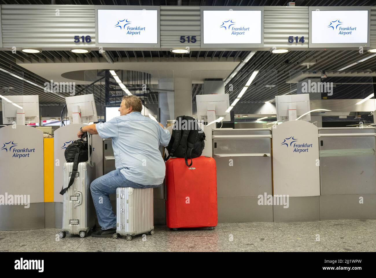 22 July 2022, Hessen, Frankfurt/Main: A passenger sits on his suitcase waiting at a counter for check-in to begin. In view of the start of the vacations in several German states, airport operator Fraport is expecting a record rush.  Around 200,000 passengers per day are expected over the weekend of July 22-24, 2022. Photo: Boris Roessler/dpa Stock Photo