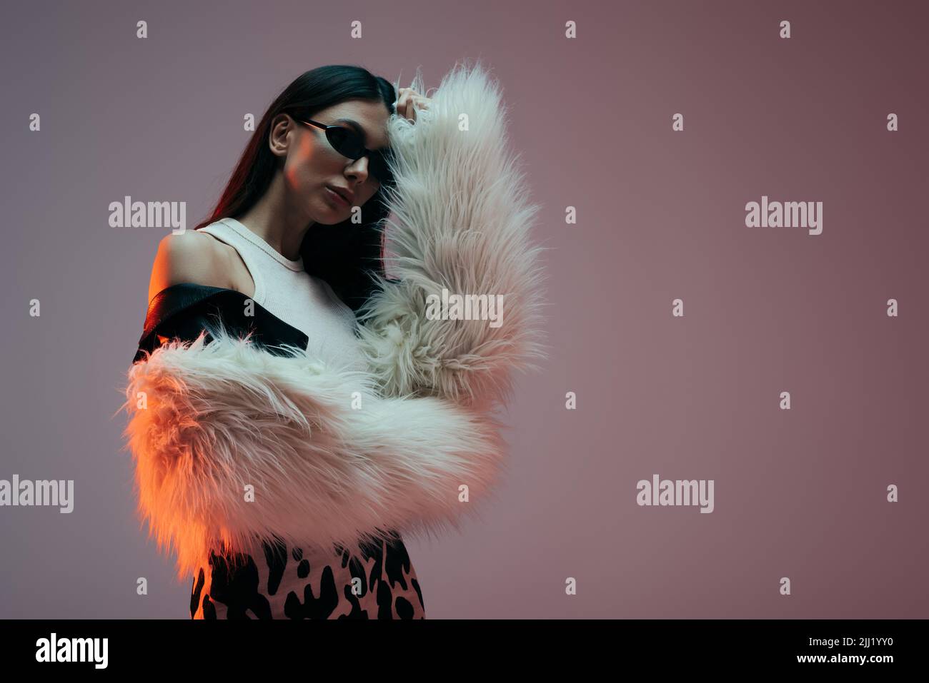 fashionable young woman in sunglasses and white faux fur jacket posing ...
