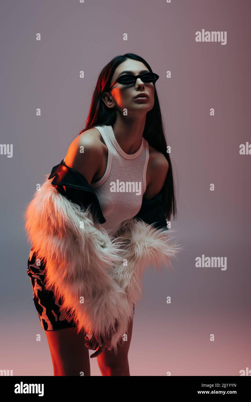 stylish young woman in sunglasses and white faux fur jacket posing on ...