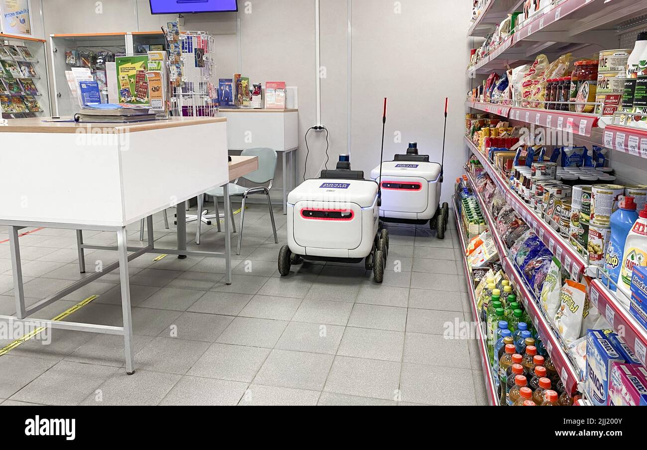 Moscow, Russia, March 2022: Two delivery robots for parcels and goods are charging from an outlet in post office next to shelves with food. Express pa Stock Photo