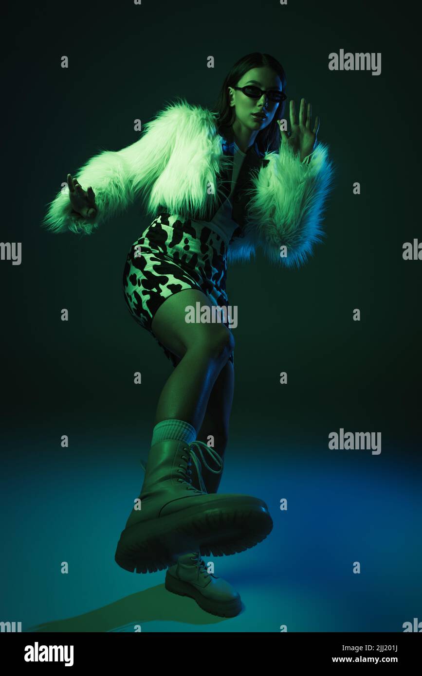 full length of stylish young woman in faux fur jacket and sunglasses ...