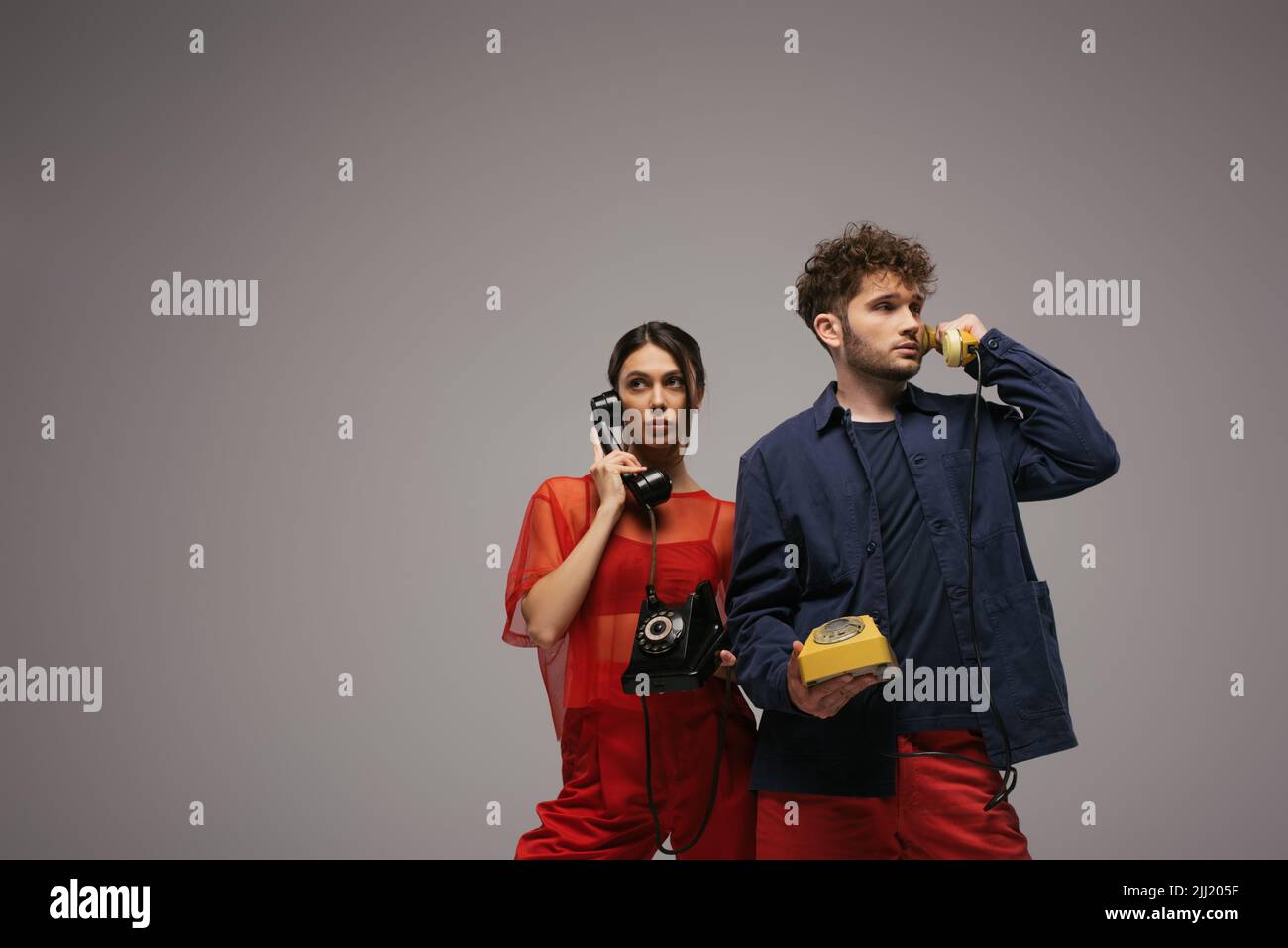 stylish young couple holding handsets and telephones isolated on grey Stock Photo