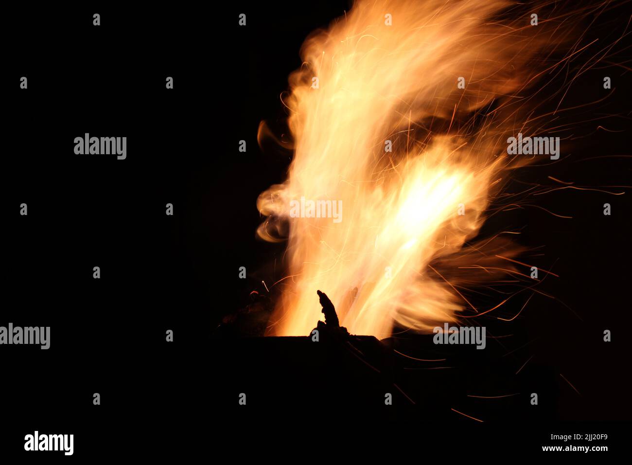 Flames of fire and sparks from firewood burning in a metal outside fireplace at night against a dark sky Stock Photo