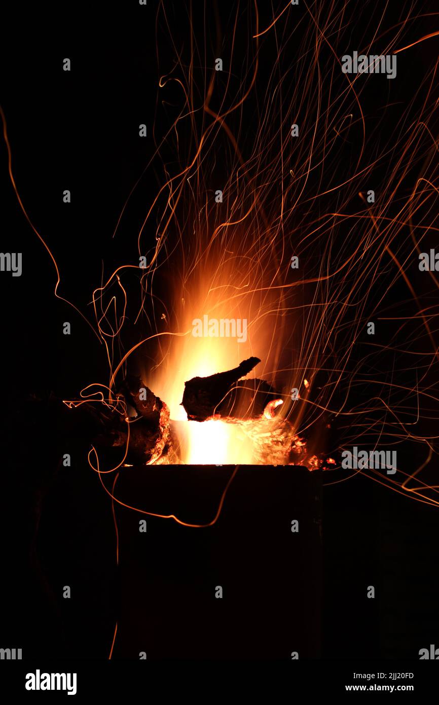 Flames of fire and sparks from firewood burning in a metal outside fireplace at night against a dark sky Stock Photo