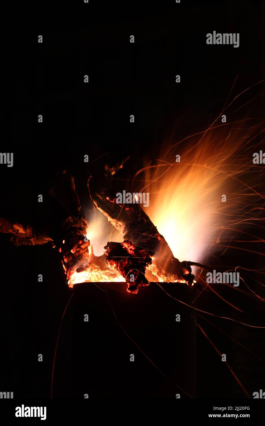 Flames of fire and sparks from firewood burning in a metal outside fireplace at night against a dark sky Stock Photo