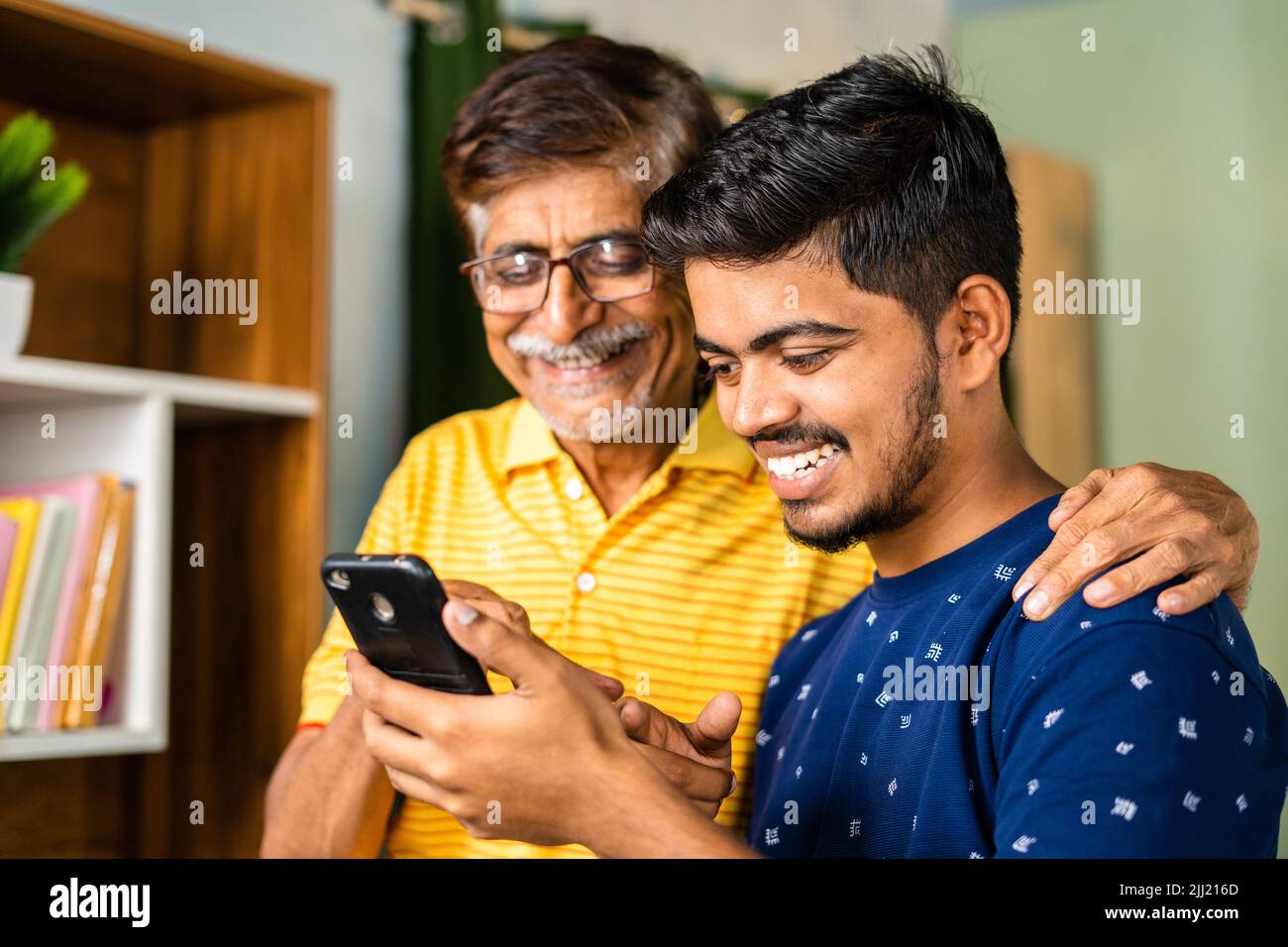 Happy smiling grandson showing new application on Mobile phone to grandfather at home - concept of social media, surfing internet and cyberspace Stock Photo