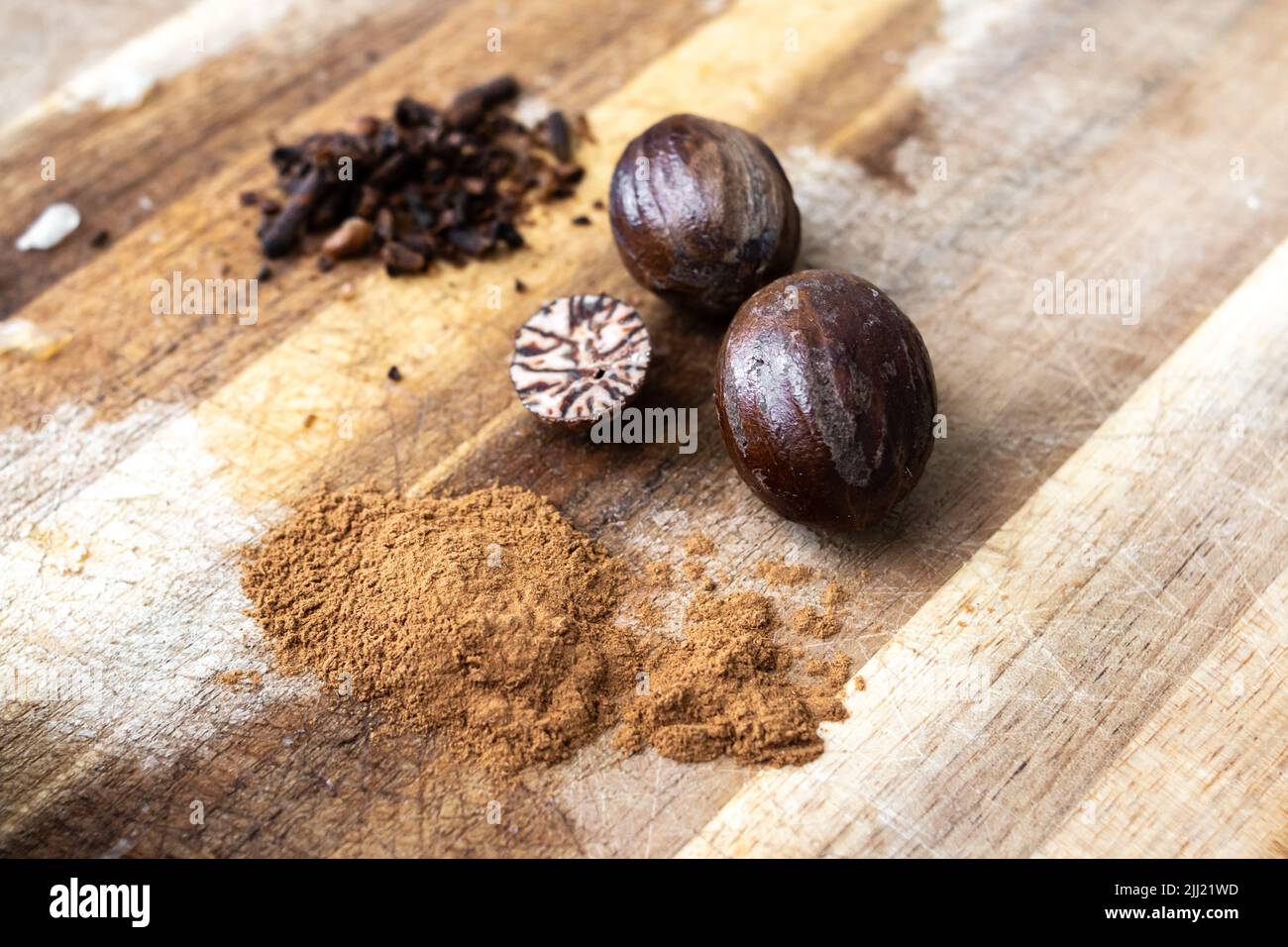 Close-up of nutmeg in its raw form on a wooden chopping block in Grenada. Includes ground nutmeg, a cross-section of a nutmeg, chopped cloves. Stock Photo