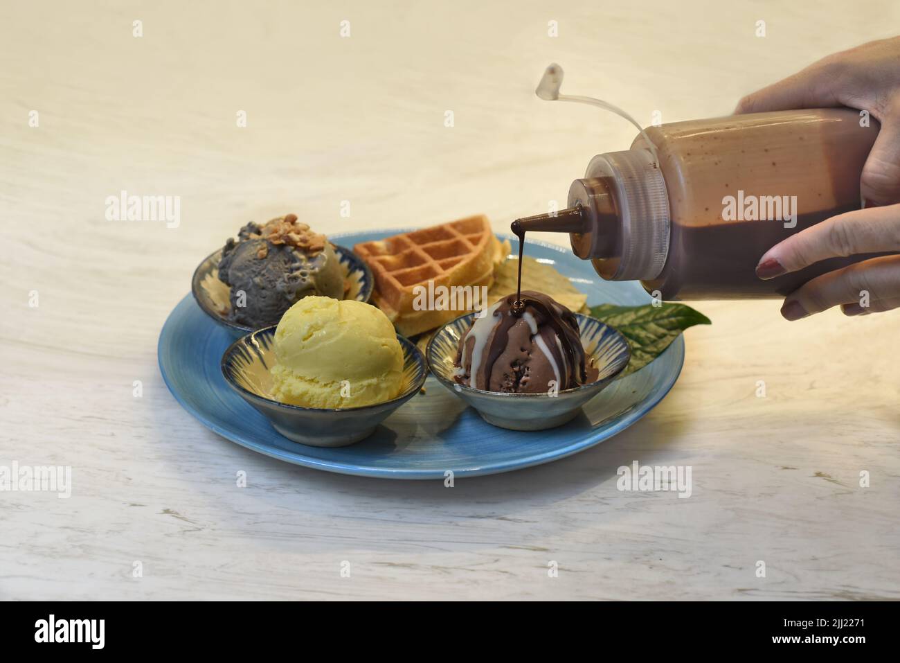 Hands pouring chocolate toping on  homemade ice cream with waffle on plate with chocolate Stock Photo