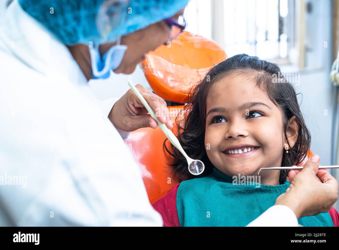 happy smiling kid looking at dentist while treating at hospital - concept of dental care, expertise and friendly hygienist. Stock Photo
