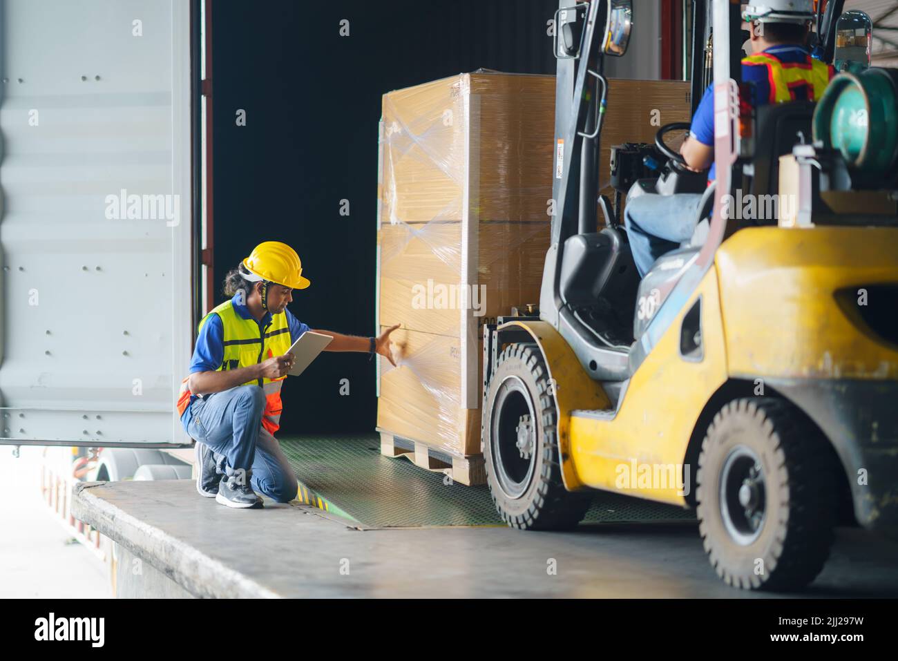 Asian forklift driver loading a shipping cargo container with a full pallet with boxes in logistics port terminal. Asian warehouse worker and safety i Stock Photo