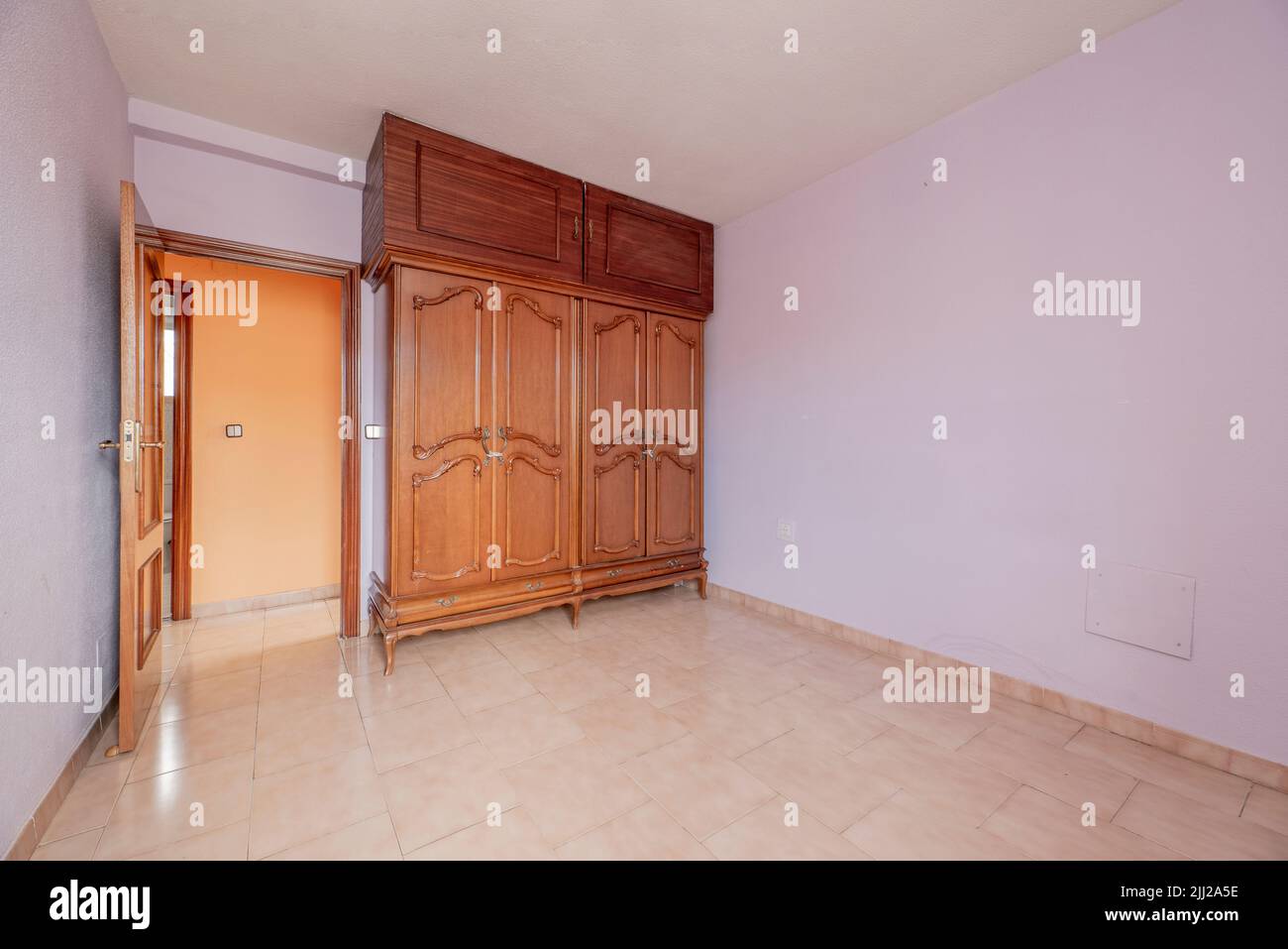 Empty room with pink stoneware floor, light purple painted walls and matching woodwork and wooden cabinets with abandoned chests Stock Photo
