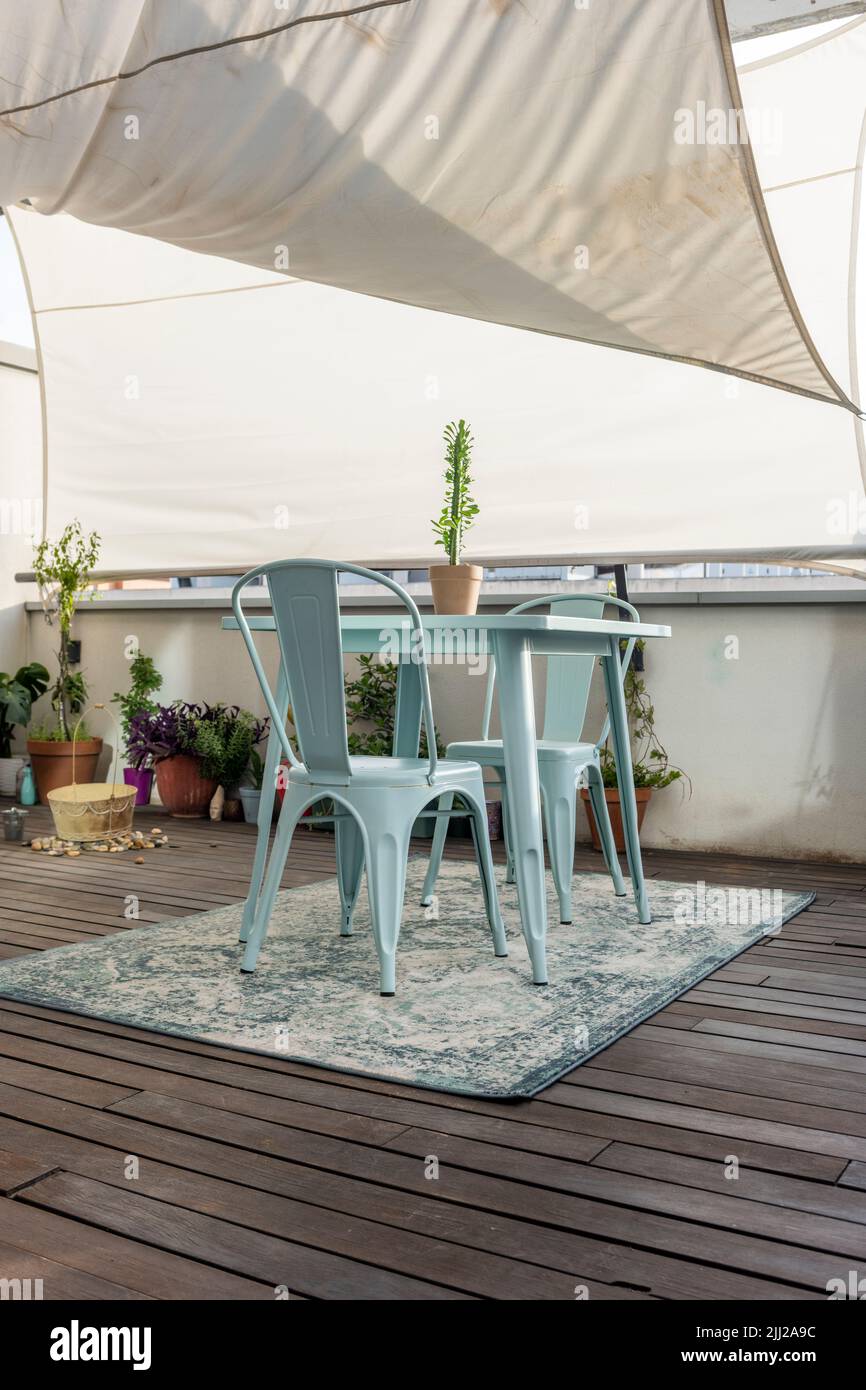 Terrace of an apartment with acacia wood flooring, decorative plants and tradescantia pallida, light blue metal table and chairs and stone pots below Stock Photo