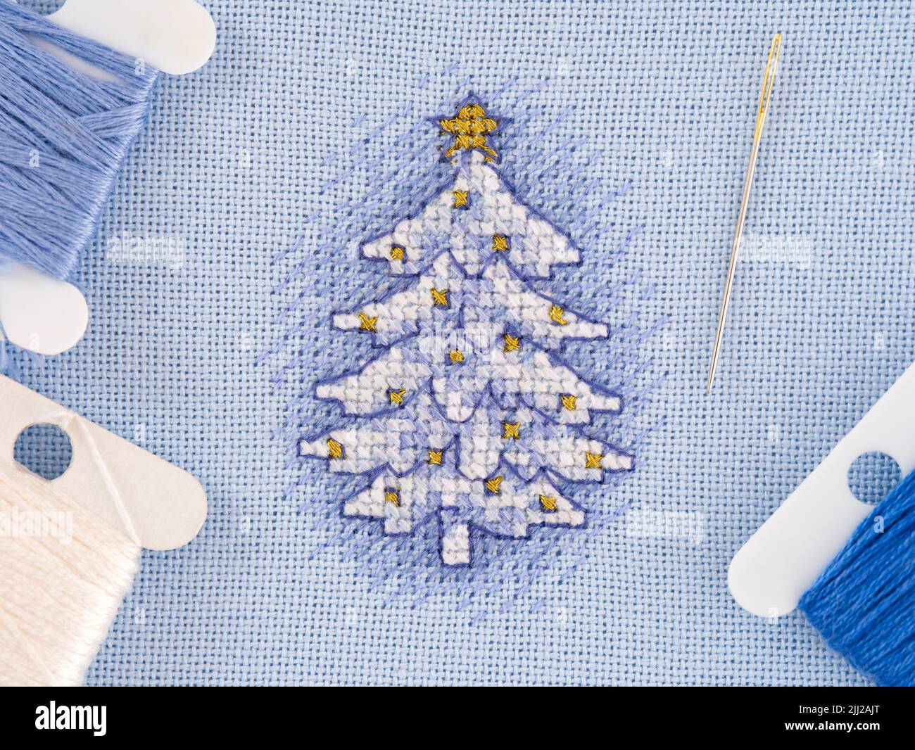 A cross stitch of a Christmas tree with blue and white threads and a needle next to it. A Christmas tree embroidered by myself. Design by Dimensions I Stock Photo