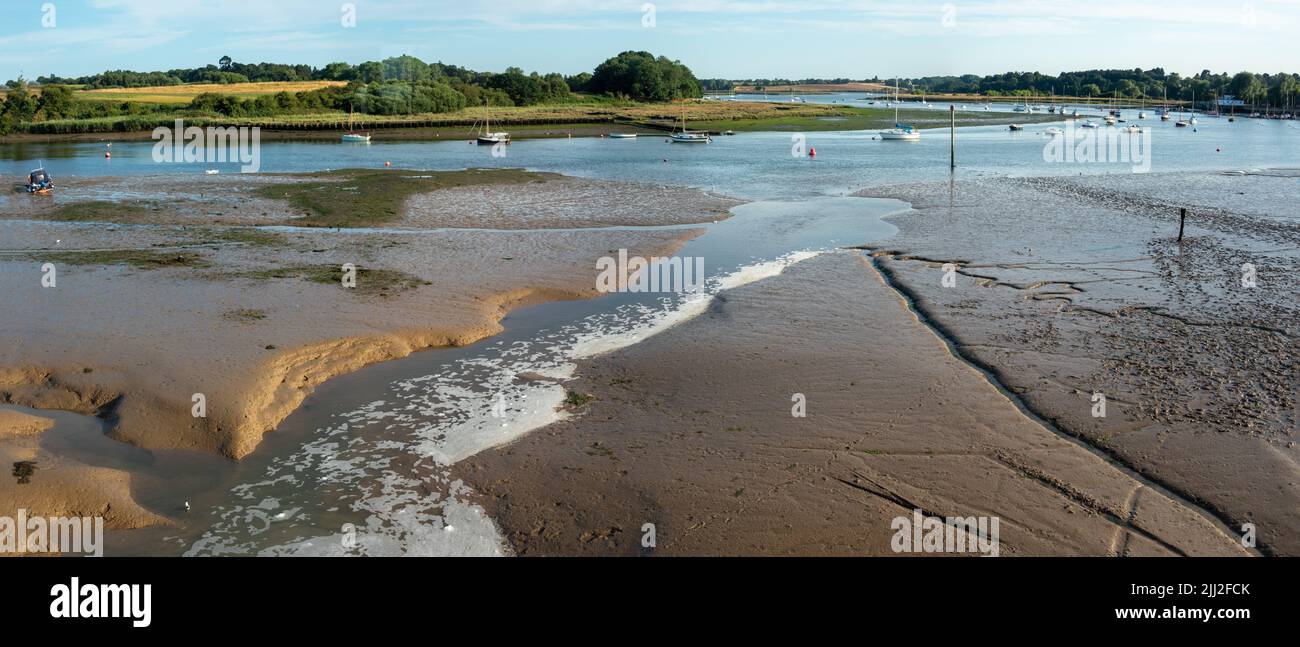 Panorama of water flowing from the Tide Mill at Woodbridge with the Deben River at low tide and boats moored in the winding river Suffolk England Stock Photo