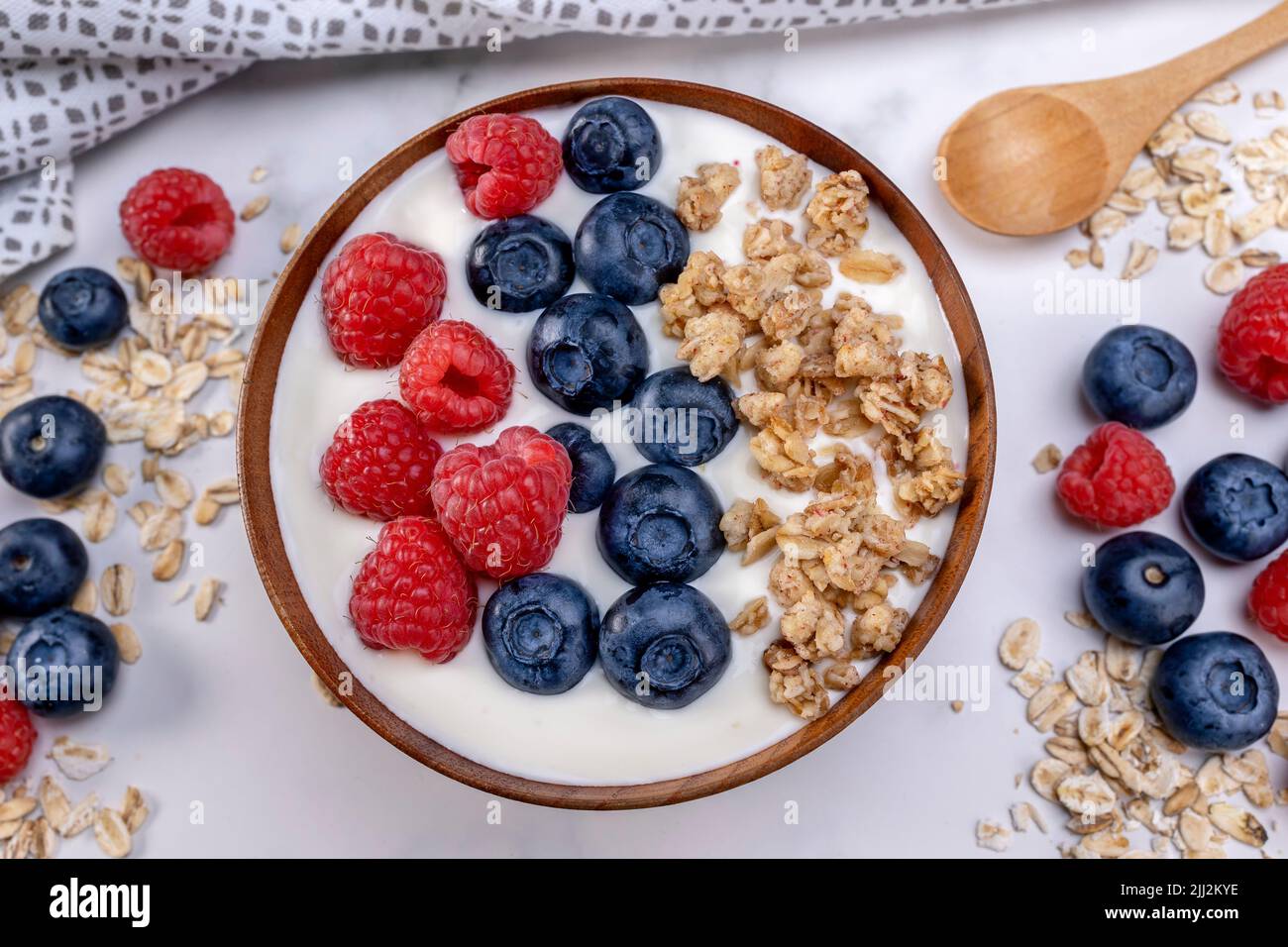 Serving a portion of yogurt with blueberry raspberry and oat flakes in a wooden bowl ready to be served. Healthy food for dieting concept. Fruit muesl Stock Photo