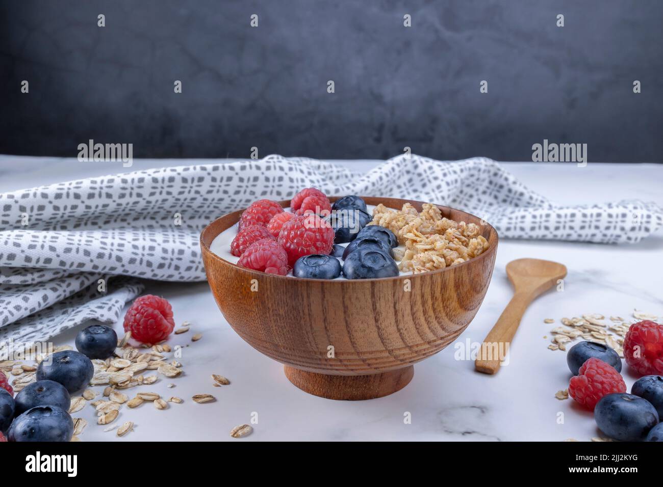 Serving a portion of yogurt with blueberry raspberry and oat flakes in a wooden bowl ready to be served. Healthy food for dieting concept. Fruit muesl Stock Photo